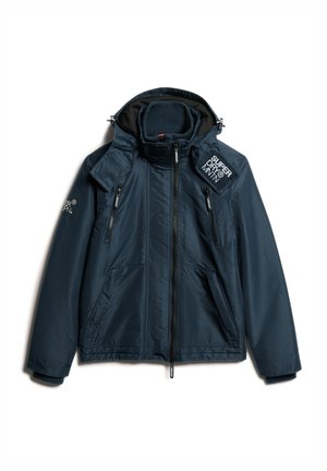 Navy blauwe jas met hoge kraag, ritszakken en een logo-opdruk. Heeft een soepele textuur en waterdicht materiaal, ontworpen voor gebruik in de buitenlucht.