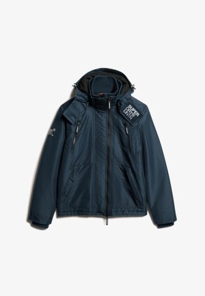 Navy blauwe jas met hoge kraag, ritszakken en een logo-opdruk. Heeft een soepele textuur en waterdicht materiaal, ontworpen voor gebruik in de buitenlucht.