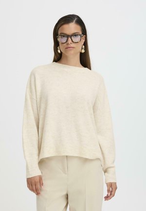 Maglione a maglia color crema con una vestibilità morbida, scollatura rotonda e polsini a coste. Abbinato a pantaloni beige chiaro.
