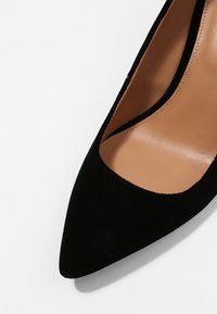 Chaussure plate pour femme à bout pointu, noire, avec semelle intérieure en cuir marron clair et finition lisse.