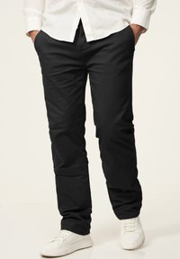 Schwarze lässige Hose aus glattem Stoff mit geradem Schnitt, ausgestattet mit Seitentaschen und kombiniert mit weißen Sneakern.