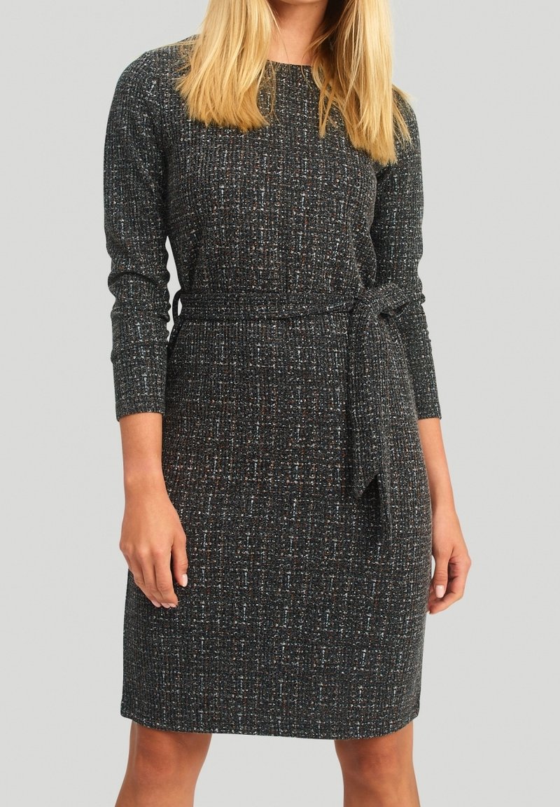 Femme portant une robe en maille gris foncé, à manches longues, longueur genou, avec un motif texturé et une ceinture nouée à la taille.