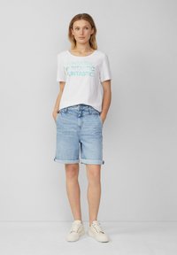 T-shirt blanc avec le texte "FUNTASTIC" en bleu clair, associé à un short en denim bleu clair replié au niveau de l'ourlet. Des baskets blanches décontractées viennent parfaire le look.