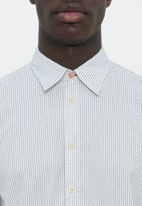 Weißes Hemd mit blauen vertikalen Streifen, ausgestattet mit einem klassischen Kragen und drei Knöpfen in Creme- und Rosatönen an der Knopfleiste.