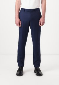 Pantalones formales azul marino con un corte ajustado, tela suave y bolsillos laterales. Destacados por un frente plano y presillas para cinturón, combinados con zapatos negros.