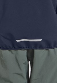 Navy fabric at the top merges into light green material below; features a horizontal white stripe, smooth texture, and elastic hem.