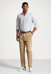 Koszula na guziki w jasnoniebieskie paski; beżowe chinosy z paskiem w paski; białe trampki z czarnymi akcentami; zegarek na lewej ręce.