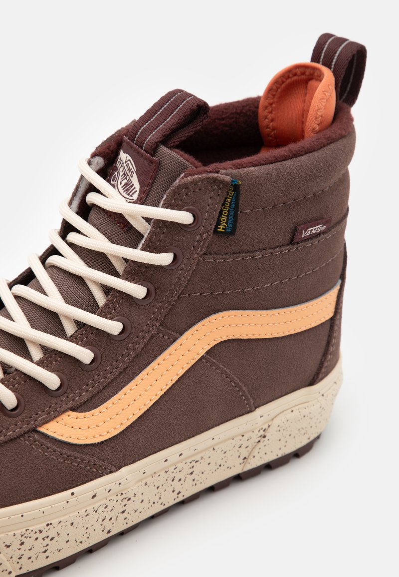 Brązowe wysokie sneakersy z gładką zamszową cholewką, pomarańczowym paskiem bocznym, kremowymi sznurowadłami, futrzanym kołnierzem i nakrapianą podeszwą. Widoczna metka HydroGuard.