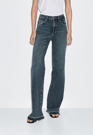 Džínové kalhoty s vysokým pasem a širokými nohavicemi v tmavě modré denimové barvě se třepeným lemem. Obsahují přední kapsy a klasické zapínání na knoflík a zip.