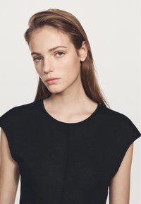 Czarny sweter z krótkimi rękawami w stylu bolerka, okrągłym dekoltem i gładką fakturą. Posiada subtelny szew wzdłuż przodu jako element ozdobny.