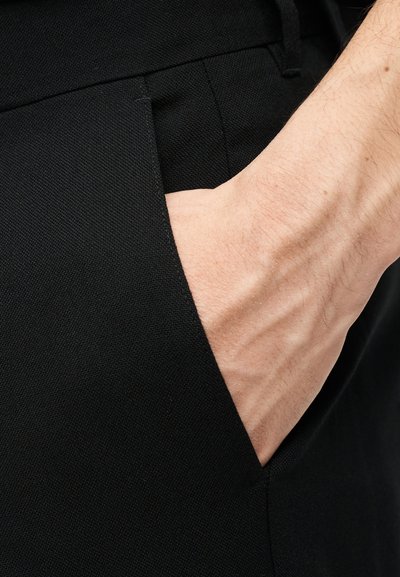 Το δεξί χέρι εισάγεται στην μπροστινή τσέπη μαύρου υφάσματος με υφή.