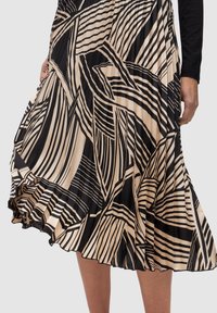 Gonna plissettata con audaci linee geometriche nere e beige, indossata da una persona che solleva leggermente il tessuto con una mano.