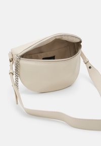 Borsa a tracolla in pelle beige con forma arrotondata, zip superiore in argento, tracolla in catena e pelle, e una singola tasca interna.