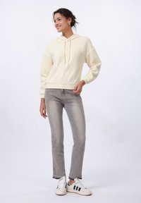 Hoodie giallo chiaro con maniche testurizzate e coulisse. Abbinato a jeans grigio chiaro e sneakers bianche con strisce nere.