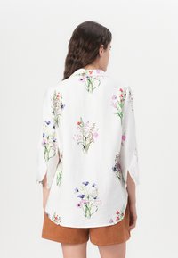 White floral blouse featuring vibrant printed flowers in pink, purple, and red, with a relaxed fit and 3/4 length sleeves.