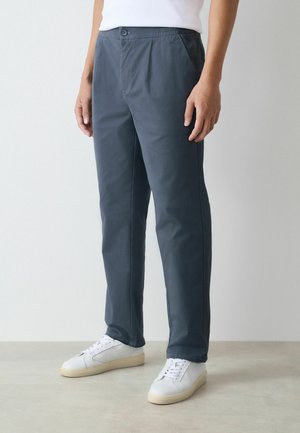 Gray, lightweight trousers with an elastic waistband and button closure, featuring a straight cut and smooth texture. Worn with white sneakers.