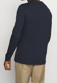 Mörkblå långärmad t-shirt med rund hals, mjuk textur och lätt krökt fåll, matchad med khakibyxor.