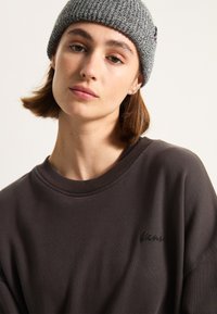 Dark gray sweatshirt with a round neck and an embroidered logo on the chest, paired with a textured knit gray beanie.