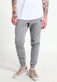 Šedé tepláky s úzkým střihem, vyrobené z měkké látky, s elastickým pasem a manžetami, kombinované s béžovými teniskami.