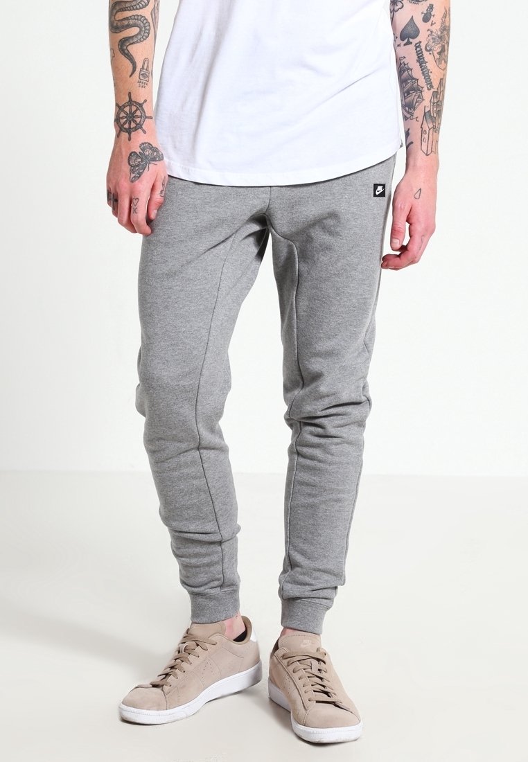 Šedé tepláky s úzkým střihem, vyrobené z měkké látky, s elastickým pasem a manžetami, kombinované s béžovými teniskami.