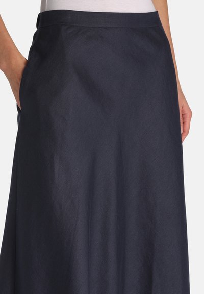 Persoană purtând o fustă în linie A de culoare bleumarin închis, cu mâinile în buzunarele laterale și un top alb, prezentată de la talie până la mijlocul coapselor, pe un fundal simplu.