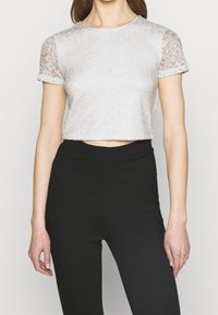 Top corto de encaje rosa claro con mangas cortas y patrón floral, cuello redondo y mangas ligeramente transparentes, combinado con pantalones negros de cintura alta.