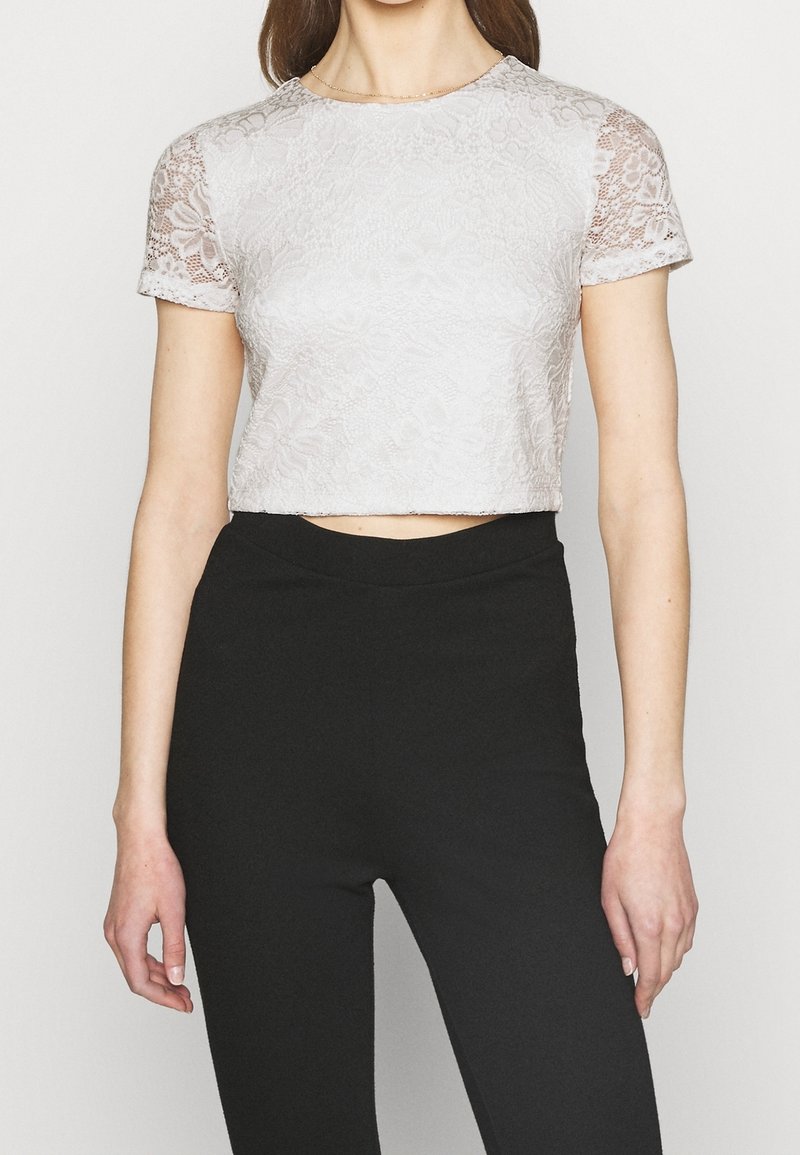 Top corto de encaje rosa claro con mangas cortas y patrón floral, cuello redondo y mangas ligeramente transparentes, combinado con pantalones negros de cintura alta.