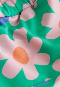 Material: glattes Gewebe. Design: lebendiger grüner Hintergrund mit großen, pastellpinkfarbenen Blumen und orangefarbenen Mitteln. Textur: weich, leicht glänzend.