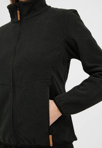 Czarna kurtka z fakturowanym górnym materiałem, zapinana na zamek z przodu, z wysokim kołnierzem i bocznymi kieszeniami. Gładkie dolne panele oraz kontrastowe akcenty metalowe.