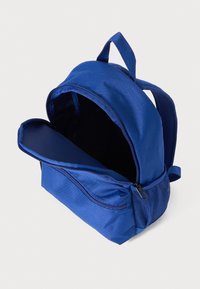 Sac à dos en tissu bleu avec un compartiment principal, une poche zippée à l'avant et des bretelles doubles. Texture lisse et forme structurée.
