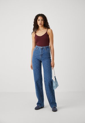 Burgundy camisole top paired with high-waisted blue denim jeans featuring white dot patterns. Model holds a light blue purse.