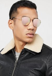 Runde, guldrammede solbriller med reflekterende, pinktonede linser. Båret med en sort læderjakke, der har en beige shearling-krave.