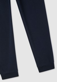 Ciemnoniebieskie spodnie dresowe z prążkowanymi mankietami na jasnoszarym tle, widok części obu nogawek.