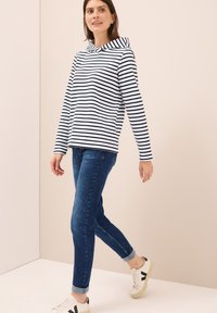 Sudadera con capucha de rayas horizontales en blanco y negro, combinada con jeans de mezclilla azul oscuro y zapatillas blancas con acentos negros.