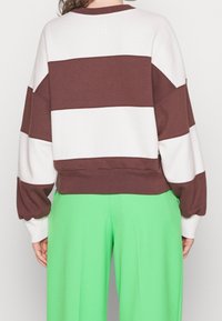 Sudadera a rayas marrón y blanca con mangas voluminosas y un dobladillo corto, combinada con pantalones verdes. Tejido suave con un ajuste holgado.