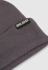 Berretto lavorato a maglia grigio con una finitura testurizzata, caratterizzato da un'etichetta in tessuto nera con il nome del marchio "SMILODOX" ricamato in bianco.