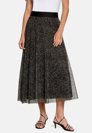 Femme portant une jupe midi imprimé zèbre noir et gris avec une ceinture noire et des sandales à talons noires à brides.