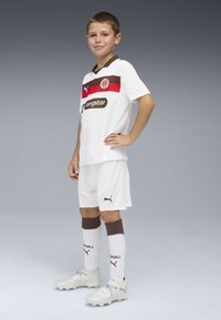 Vit fotbollskit med röda och bruna accenter, med en logotyp och sponsorstextfield. Bruna randiga strumpor och silverfärgade fotbollsskor.