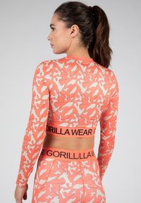 Langere mouwen sports tops in koraal met een beige dierenprint en een elastische tailleband met het "GORILLA WEAR" logo. Glad, rekbaar materiaal.