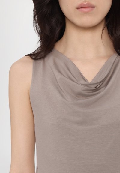 Ermeløs topp med drapert hals i lyse taupe stoff. Glatt tekstur med subtil draperingsdetalj nær halsen. Minimalistisk design, ingen synlig maskinvare.
