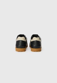 Black leather athletic shoes with a tan rubber sole, featuring a cream accent ankle area and black heel tab. Textured finish on the material.