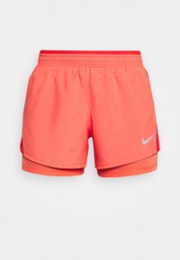 Pantalones cortos deportivos color coral con una capa interna, cintura elástica y un logo reflectante. Tela suave y detalle de la cintura en contraste rojo.