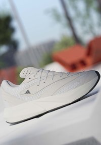 Baskets blanches de sport avec dessus en maille et synthétique, semelle intermédiaire en mousse, et semelle extérieure en caoutchouc noire, présentées à l'extérieur sur une surface blanche.