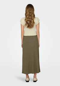 Gebreide crèmekleurige top met korte gerimpelde mouwen, gecombineerd met een lange olijfgroene rok. Model staat in neutrale schoenen, gezien vanuit de achterkant.