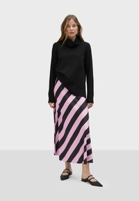 Svart koftetröja med krage som hänger över axlarna, parat med en satinkjol i rosa och svarta ränder. Modellen bär svarta platta skor med remmar.