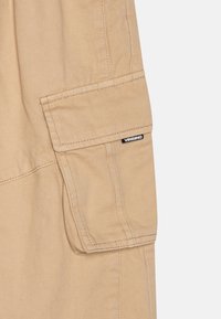Shorts cargo beiges avec une poche latérale, fabriqués en tissu durable. Présente des coutures visibles et une étiquette de marque noire étiquetée "Vingino".