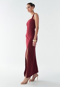 Bordo spalvos ribuota maxi suknelė su liekninančia silueto forma, šoninėmis skeltukėmis ir plonomis petnešėlėmis, derinama su dirželiais puoštomis smėlio spalvos aukštakulnėmis basutėmis.