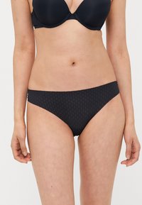 Zwarte bikinionder met een textuurpatroon, medium bedekking en een zachte elastische tailleband. De stof lijkt rekbaar en duurzaam.