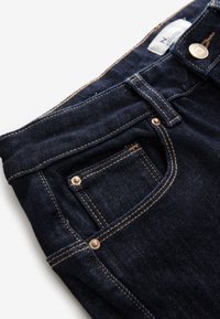 Tmavomodré džínsy z denimu s viditeľnou prednou kapsou, malou mincovou kapsou, kovovými nitmi a svetlohnedým prešívaním.