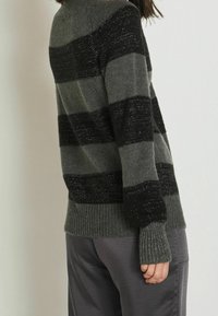 Pull en tricot gris avec des rayures horizontales noires et argentées. Les poignets et l'ourlet côtelés affichent une finition texturée, avec un design à coupe décontractée.